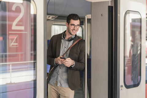 Lächelnder junger Mann mit Mobiltelefon im Nahverkehrszug, lizenzfreies Stockfoto