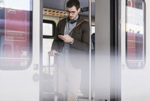 Junger Mann benutzt Mobiltelefon im Nahverkehrszug - UUF16825