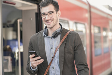 Lächelnder junger Mann mit Mobiltelefon im Nahverkehrszug - UUF16828