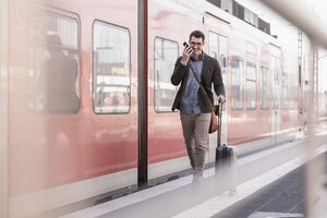 Fröhlicher junger Mann mit Handy auf dem Bahnsteig entlang eines Nahverkehrszugs - UUF16831