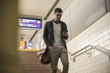 Young man with cell phone walking down stairs at the station - UUF16840