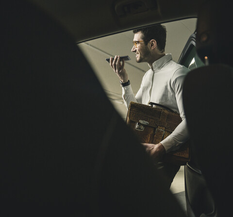 Smiling young man with bag using cell phone at a car stock photo