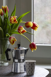 Espressokanne und Tasse auf einem Tisch mit Tulpenstrauß im Hintergrund - MELF00203