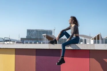 Junge Frau, die auf einer Mauer sitzt und über die Stadt blickt - AFVF02605