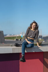 Young woman sitting on a wall listening music with headphones on her smartphone - AFVF02606