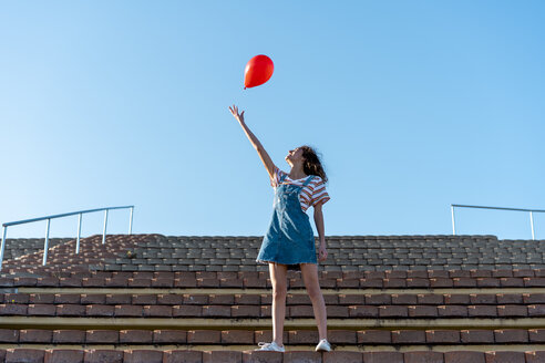Junge Frau, die auf einem Granstand steht und einen roten Luftballon loslässt - AFVF02616