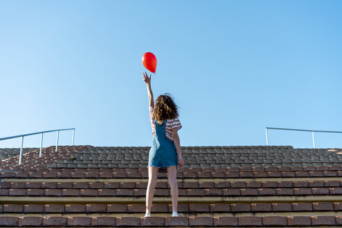 Junge Frau, die auf einem Granstand steht und einen roten Luftballon loslässt - AFVF02617