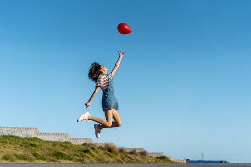 Springende junge Frau, die einen roten Luftballon loslässt - AFVF02621