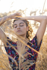 Young woman standing in meadow, enjoying the sun - AFVF02625