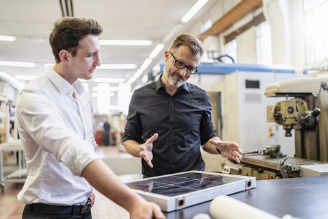 Zwei Kollegen arbeiten in einer Fabrik an einer Solarzelle, lizenzfreies Stockfoto