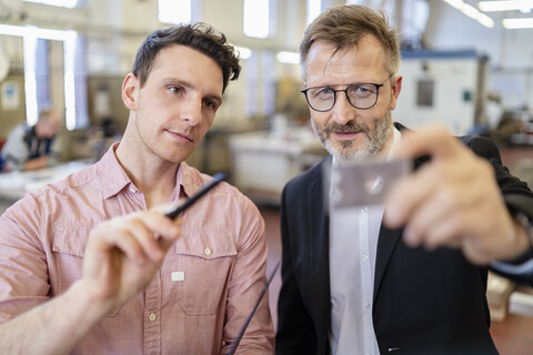 Zwei Männer in einer Fabrik prüfen ein Werkstück, lizenzfreies Stockfoto