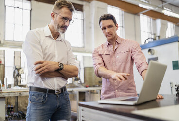 Two colleagues in factory discussing at laptop - DIGF06259