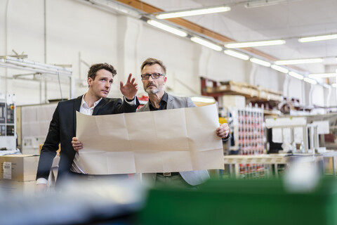 Zwei Geschäftsleute besprechen einen Plan in einer Fabrik, lizenzfreies Stockfoto