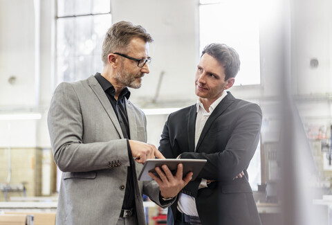 Two businessmen with tablet discussing in a factory stock photo