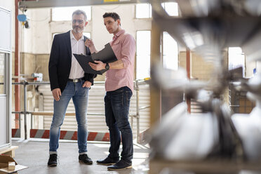 Two men with clipboard talking in factory warehouse - DIGF06303