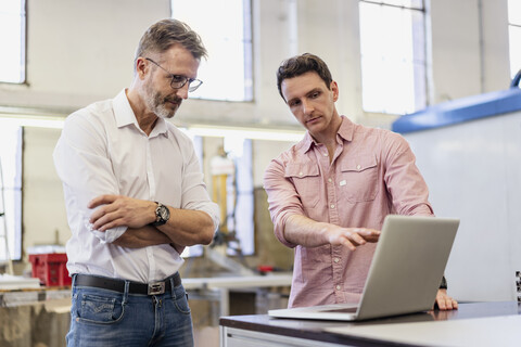 Two colleagues in factory discussing at laptop stock photo