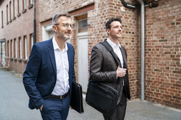 Zwei lächelnde Geschäftsleute gehen an einem alten Backsteingebäude vorbei - DIGF06333