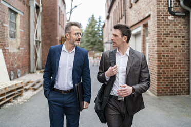 Two businessmen walking and talking at an old brick building - DIGF06336