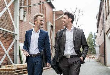 Zwei lächelnde Geschäftsleute, die vor einem alten Backsteingebäude spazieren gehen und sich unterhalten - DIGF06337