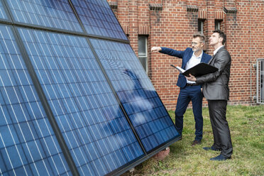 Zwei Geschäftsleute unterhalten sich vor einem Backsteingebäude mit Sonnenkollektoren - DIGF06339