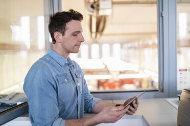 Businessman using tablet at the window with factory background - DIGF06358