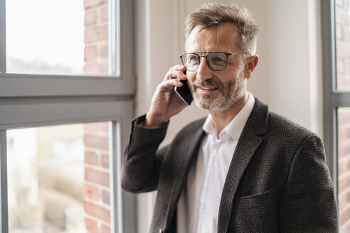 Geschäftsmann am Handy am Fenster im Büro - DIGF06359