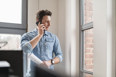 Businessman on cell phone at the window in office - DIGF06365