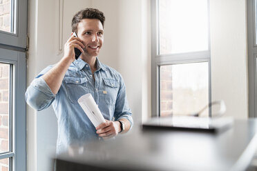 Lächelnder Geschäftsmann am Mobiltelefon am Fenster im Büro - DIGF06366