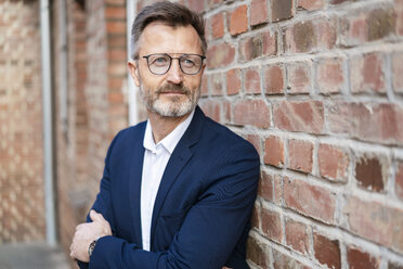 Portrait of businessman at brick wall looking sideways - DIGF06383