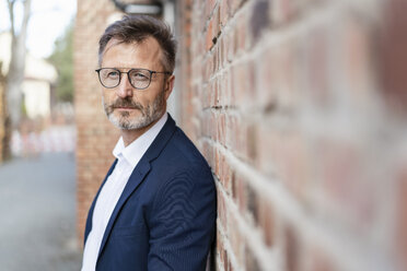 Portrait of businessman at brick wall looking sideways - DIGF06384