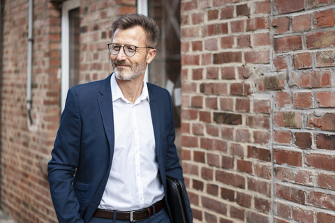 Smiling businessman walking along brick building stock photo