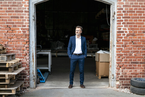 Businessman standing at old warehouse looking away stock photo