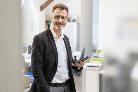 Porträt eines lächelnden Geschäftsmannes, der ein Tablet im Büro benutzt, lizenzfreies Stockfoto