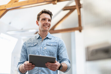 Porträt eines lächelnden jungen Geschäftsmannes, der ein Tablet im Büro benutzt - DIGF06399