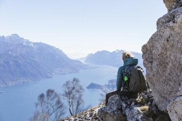 Italien, Como, Lecco, Frau auf Wandertour in den Bergen oberhalb des Comer Sees, auf einem Felsen sitzend und die Aussicht genießend - MRAF00383