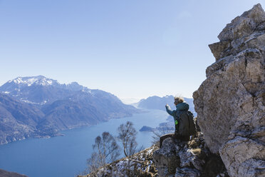 Italien, Como, Lecco, Frau auf Wandertour in den Bergen oberhalb des Comer Sees, auf einem Felsen sitzend und die Aussicht genießend - MRAF00384