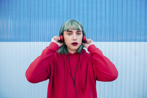 Porträt einer jungen Frau mit blau gefärbtem Haar, die mit Kopfhörern Musik hört, lizenzfreies Stockfoto