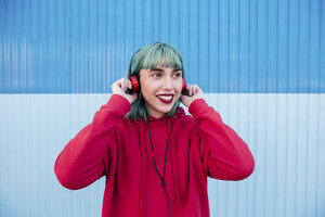 Porträt einer lächelnden jungen Frau mit blau gefärbtem Haar, die mit Kopfhörern Musik hört - LOTF00064