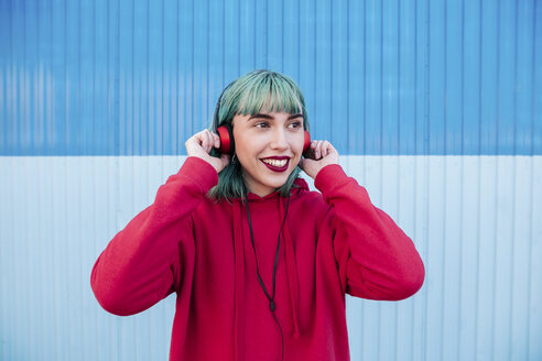 Portrait of smiling young woman with blue dyed hair listening music with headphones - LOTF00064