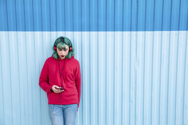Junge Frau mit blau gefärbten Haaren hört Musik mit Kopfhörern, während sie auf ihr Smartphone schaut - LOTF00068