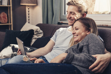 Happy young couple using tablet on couch at home - SEBF00086