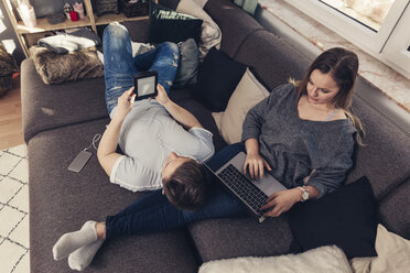 Junges Paar entspannt sich auf dem Sofa und benutzt Notebook, Smartphone und E-Book-Reader - SEBF00088