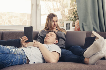 Young couple relaxing on sofa and using notebook, smartphone and ebook reader - SEBF00089