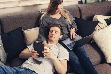 Junges Paar entspannt sich auf dem Sofa und benutzt Notebook, Smartphone und E-Book-Reader - SEBF00092