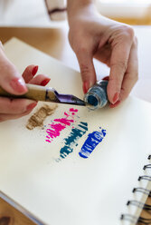 Frauenhand, die Farbpigmente auf ein Malbuch aufträgt - MGOF03982