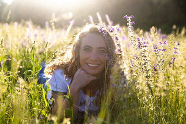 Portrait of happy woman lying on flower meadow at evening twilight - SARF04172