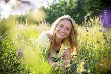 Portrait of happy blond woman lying on flower meadow in summer - SARF04174