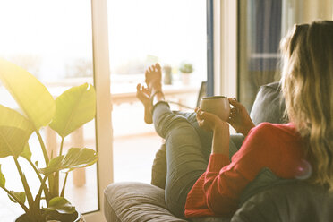 Woman relaxing in armchair at home holding coffee cup - SBOF01894