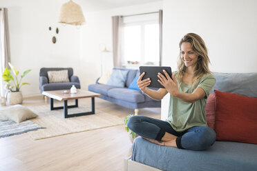 Glückliche Frau, die zu Hause auf der Couch sitzt und ein Tablet benutzt - SBOF01908