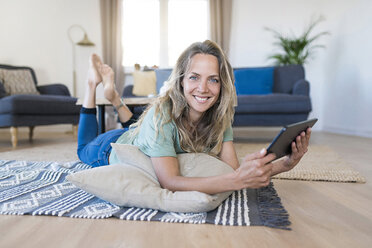 Porträt einer lächelnden Frau, die zu Hause auf dem Boden liegt und ein Tablet benutzt - SBOF01909